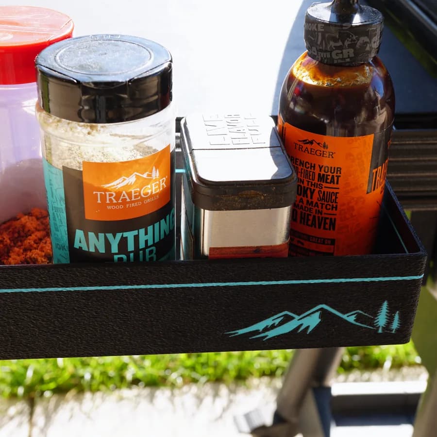 A printed Traeger rail tray holding spice jars and sauce on a grill